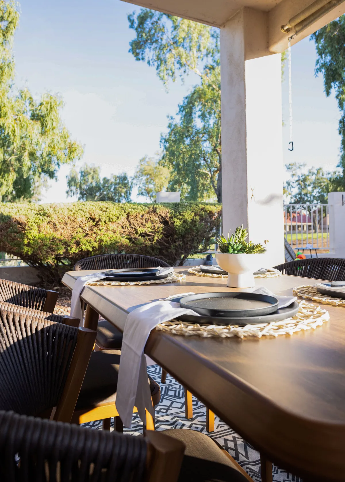 An inviting outdoor dining area set with elegant place settings and a succulent centerpiece, surrounded by lush greenery. The table is ready for a group to gather for a sunset meal, reflecting the home’s suitability for socializing and sophisticated gatherings.