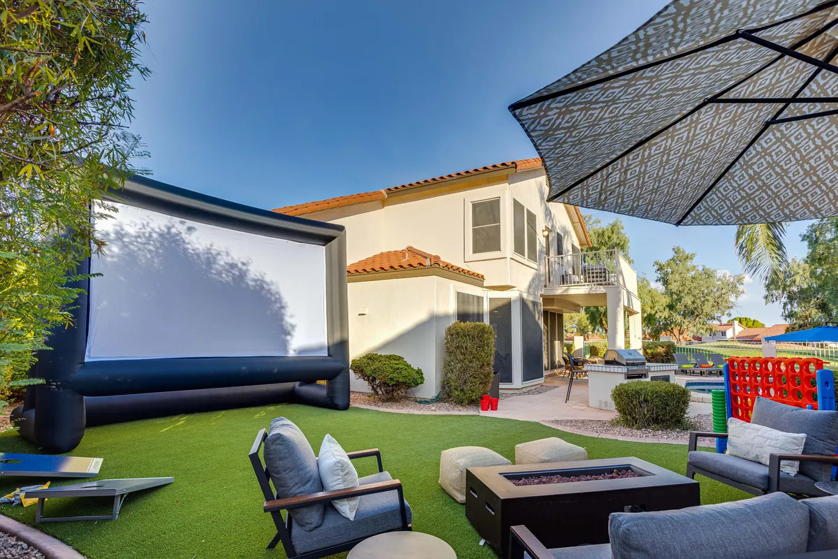 This exterior image features an inflatable movie screen set up in the backyard, surrounded by an outdoor seating area, fire pit, and a large umbrella. The relaxed setting under open skies is perfect for group gatherings and outdoor activities.