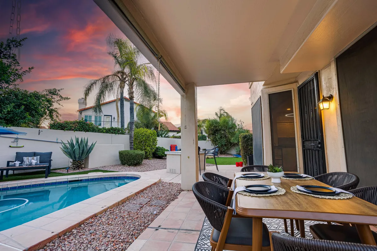 A well-set outdoor dining table with place settings overlooking the pool, surrounded by a landscaped garden and inviting seating area. The space is perfect for casual meals or festive gatherings in the open air.