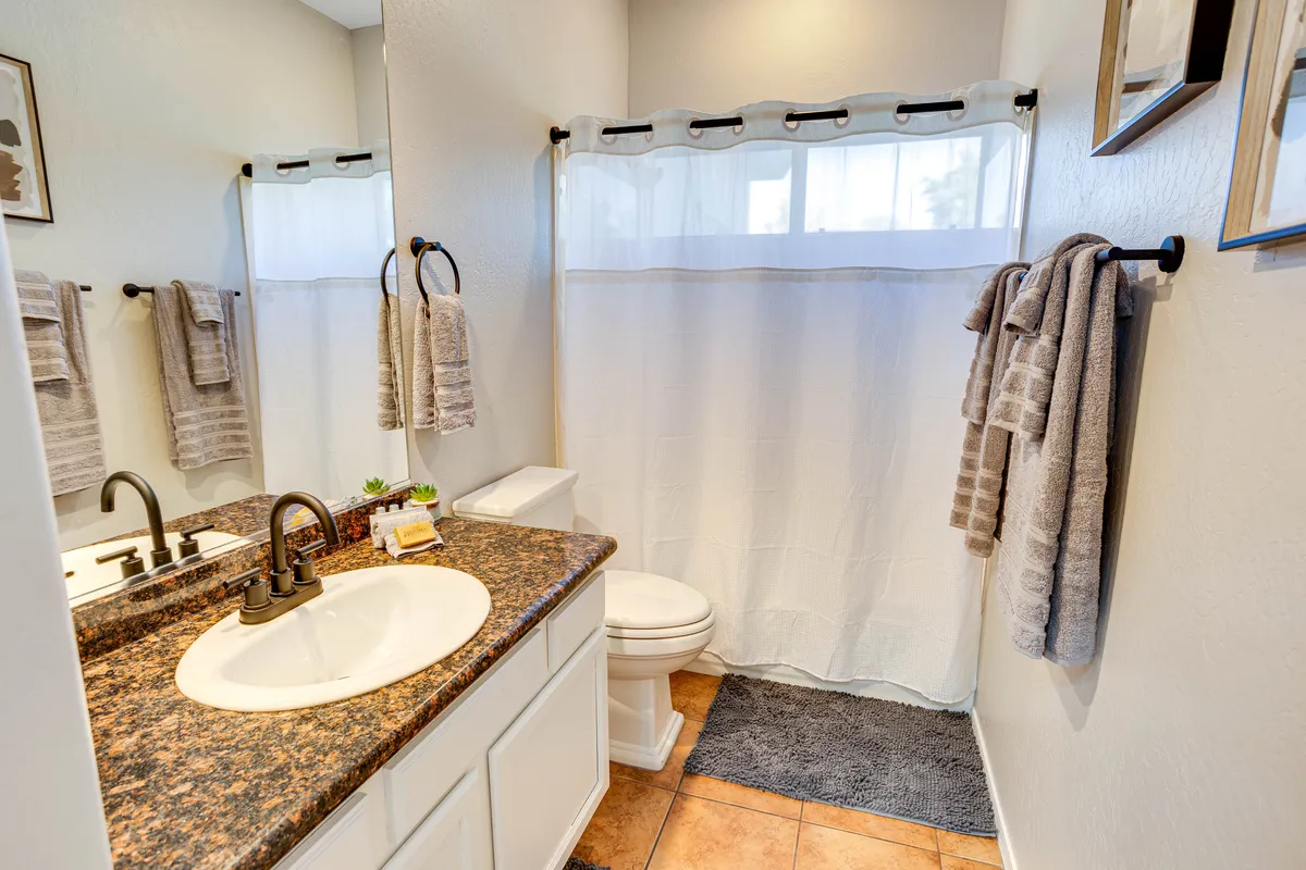 A modern bathroom with an elegant granite countertop, oval sink, plush towels, mirrors, and a shower curtain. The space is bright, clean, and thoughtfully designed for relaxation and self-care.