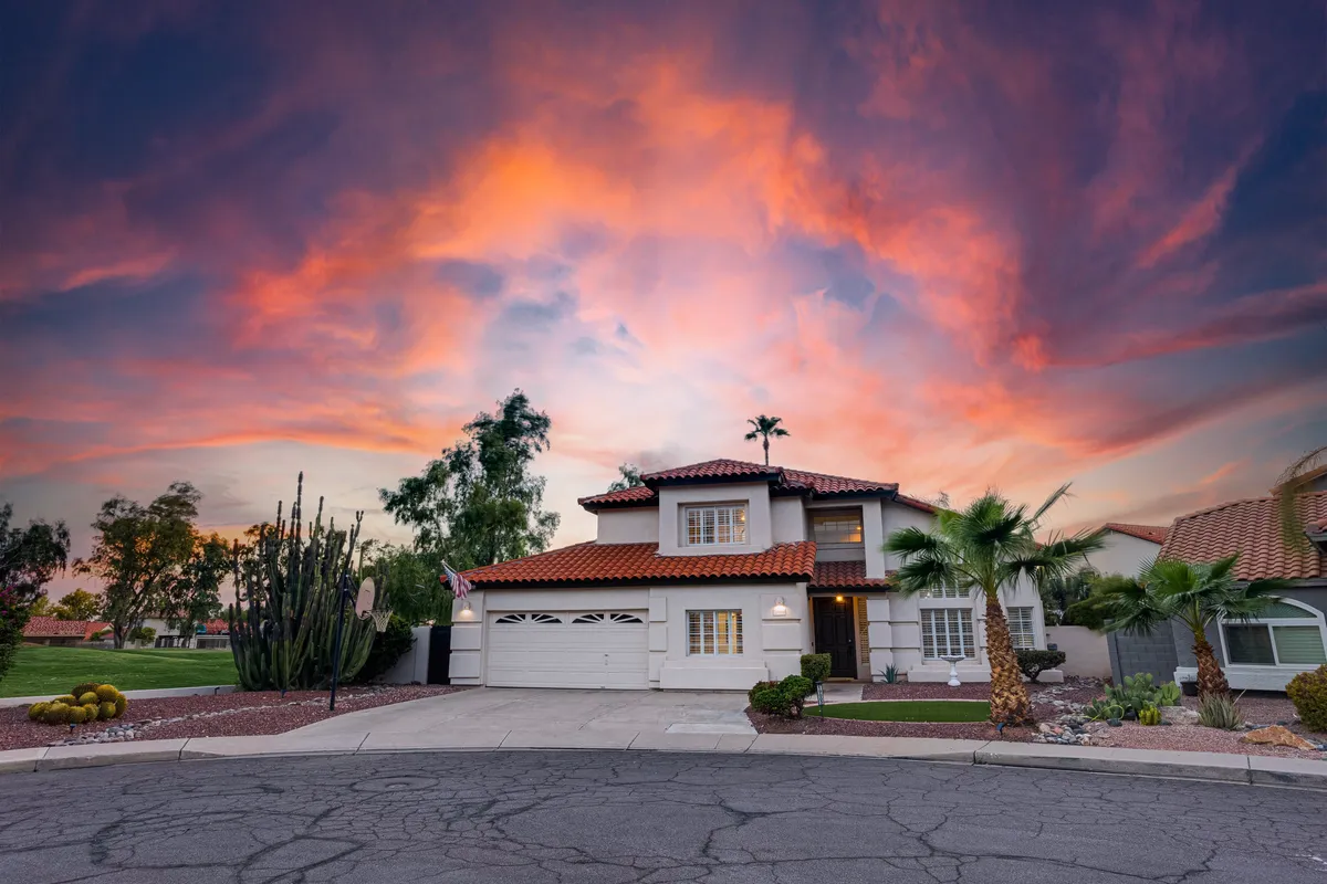 A wide-angle exterior shot of the house set against a vibrant sky, with palm trees and cacti in the foreground. The welcoming porch hints at the inviting vibe of the home and its surroundings, providing a strong sense of arrival and neighborhood context.