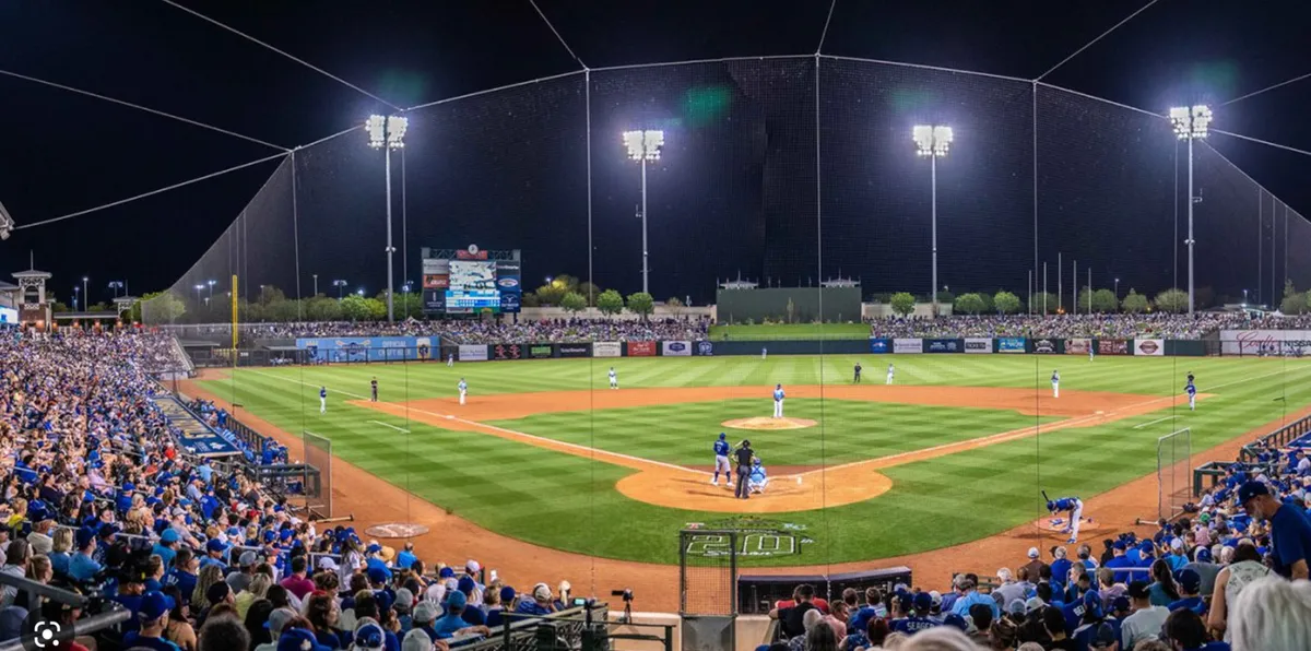 A vibrant exterior shot of a baseball diamond filled with players, a cheering crowd, and a scoreboard, capturing the excitement and communal spirit of a live sporting event.