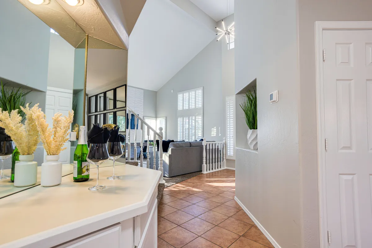 An inviting bar area with a variety of drinks, decorative plants, a staircase leading to an upper level, and a sofa situated in the adjoining living space. The design encourages socializing over drinks and relaxation.
