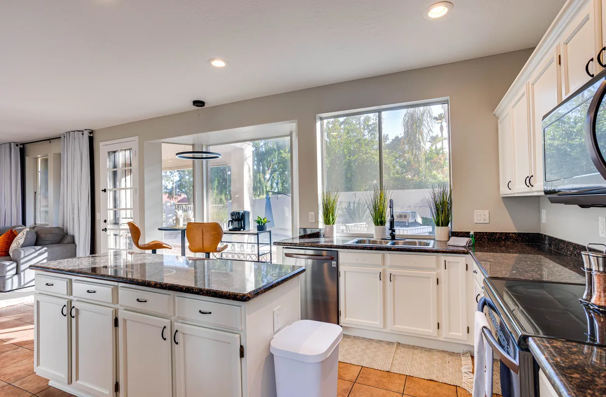 A wide-angle view of the kitchen and dining area, highlighting a kitchen island, large windows, modern appliances, and comfortable dining chairs. Natural light streams in, illuminating a space designed for both meal prep and gathering.