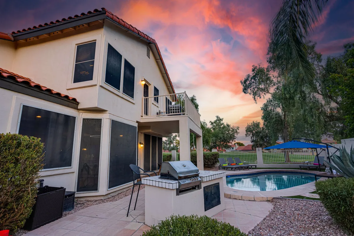 A sparkling swimming pool with a barbecue grill, a balcony, and a sky painted with sunset colors. The setup is perfect for group relaxation and entertaining after a day spent on the course or at nearby sports venues.